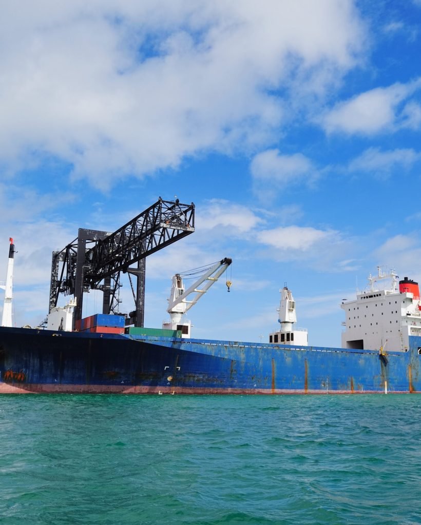 Cargo ship at Miami harbor with crane and blue sky over sea.